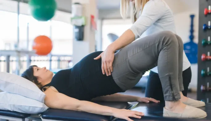 Physical therapist guiding a patient through a supported pelvic floor exercise on a treatment table